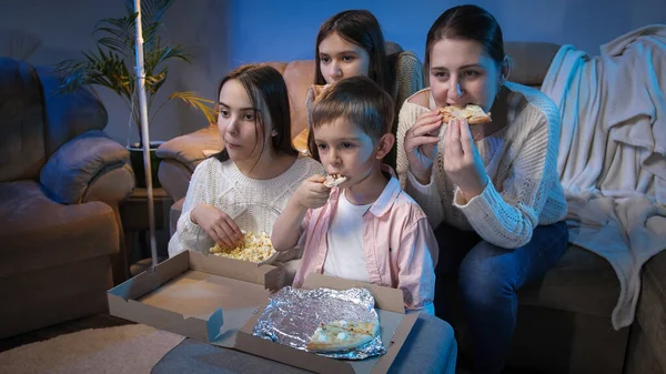 Большая семья смотрит вечернее телешоу или кино на диване и ест пиццу и попкорн. — стоковое фото