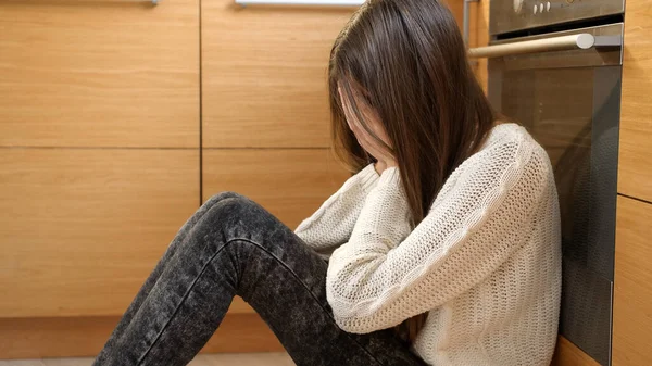 Chica adolescente llorando sentada en el suelo en la cocina. Problemas mentales y depresión de los adolescentes —  Fotos de Stock