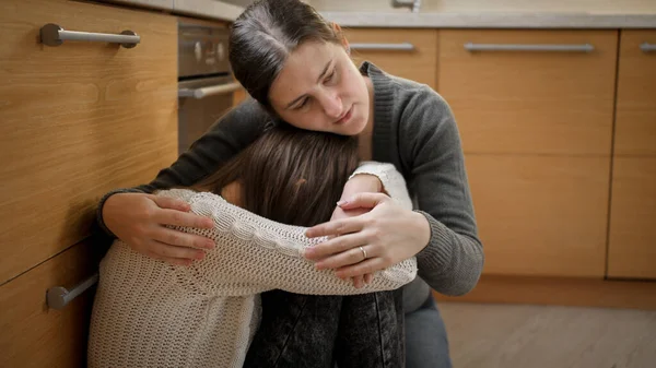 Rozrušená plačící puberťačka sedící na podlaze a objímající matku. Koncept domácího násilí a rodinné agrese a deprese teenagerů. — Stock fotografie