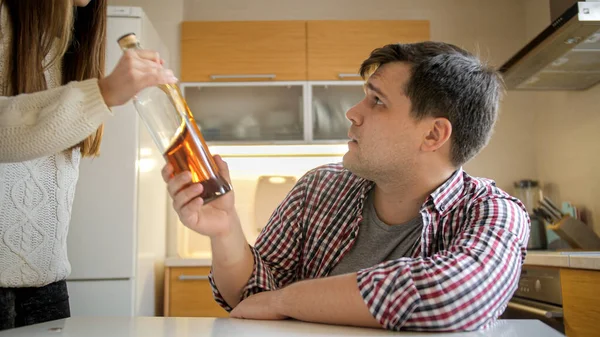 Young woman taking bottle of alcohol from male alcoholic drinking spirits on kitchen — Stock Photo, Image