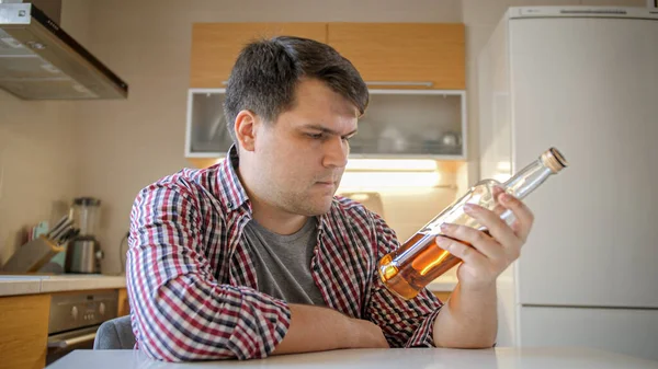 Upset man in depression looking on bottle of alcohol drink on kitchen. — Stock Photo, Image