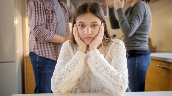 10代の少女がカメラを見て、両親が紛争中に叫んで叫ぶのを無視する姿。家庭内暴力、紛争、関係の問題 — ストック写真