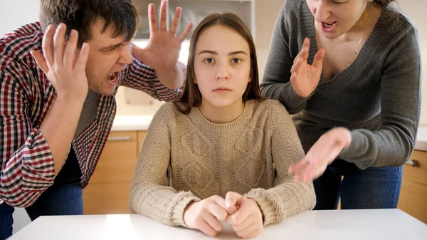 Padre y madre gritando y gritando a la hija adolescente sentada detrás de la mesa en la cocina. Violencia familiar, conflictos y problemas de relación — Foto de Stock