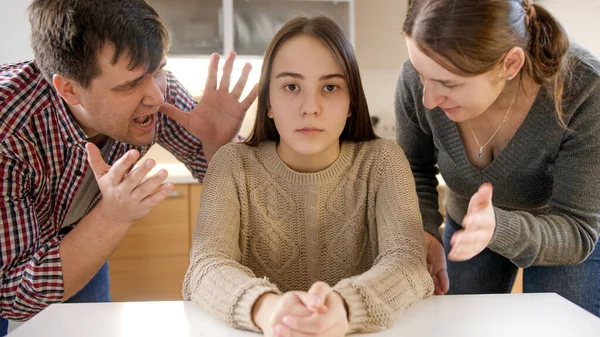 Los padres gritando y gritando a la hija adolescente sentada detrás de la mesa y mirando en la cámara — Foto de Stock
