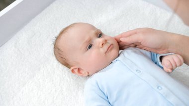 Annesi masaj yaparken ve onunla oynarken, sehpada uzanan tatlı bir erkek bebek. Hijyen, bebek bakımı ve sağlık hizmetleri kavramı