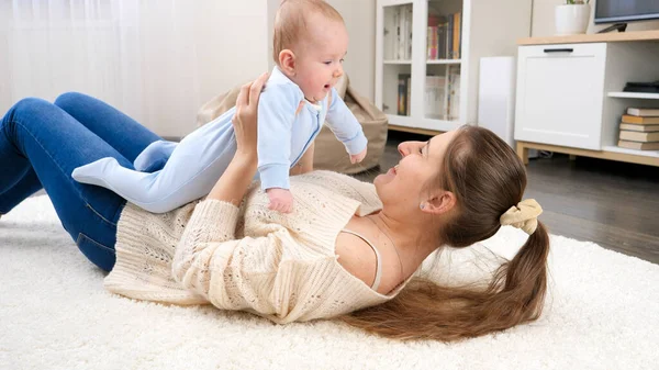 Szczęśliwa uśmiechnięta matka z małym synkiem leżącym na podłodze w salonie i bawiącym się. Pojęcie szczęścia rodzinnego i rozwoju dzieci — Zdjęcie stockowe