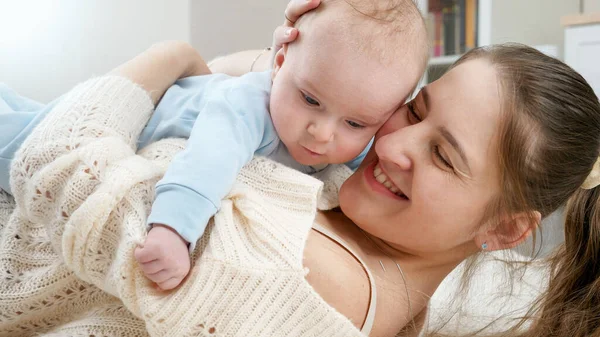 Portrait of smiling young mother hugging and embracing her little baby son while lying on floor. Concept of family happiness and child development — Stock Photo, Image