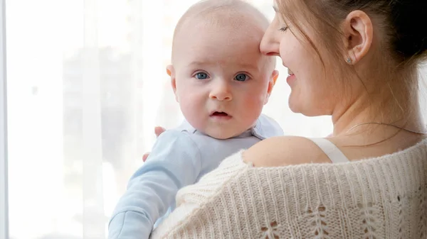 Closeup portrait of baby and mother face hugging and embracing at big window at home. Concept of family happiness and child development — Stock Photo, Image