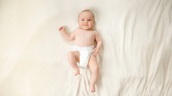 Top kilátás a kisfiú pelenkás feküdt puha fehér takaró az ágyon. — Stock Fotó