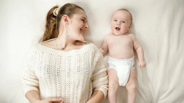 Feliz menino sorridente em fraldas e mãe deitada na cama e olhando um para o outro. Conceito de parentalidade, higiene do bebê e desenvolvimento infantil. — Fotografia de Stock