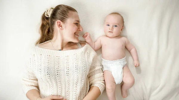 Liebenswert lächelndes Baby, das die im Bett liegende Mutter anlächelt. Konzept von Elternschaft, Babyhygiene und kindlicher Emotion — Stockfoto