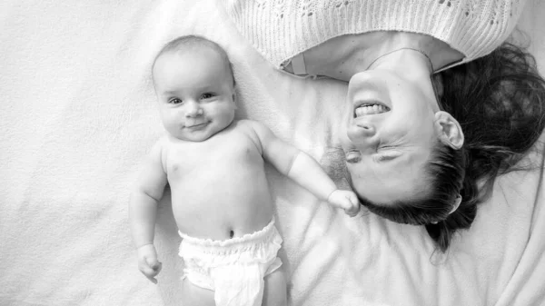 Black and white portrait of smiling mother with little baby lying on bed — Stock Photo, Image