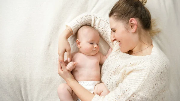Mère souriante attentionnée couchée avec son petit fils en couches et le nourrissant doucement. Concept de parentalité, d'hygiène du bébé et de garde d'enfants — Photo