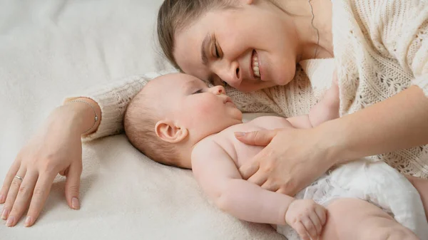 Lindo niño tocando a su sonriente madre acostada a su lado en la cama. Concepto de crianza, cuidado del bebé y felicidad familiar — Foto de Stock