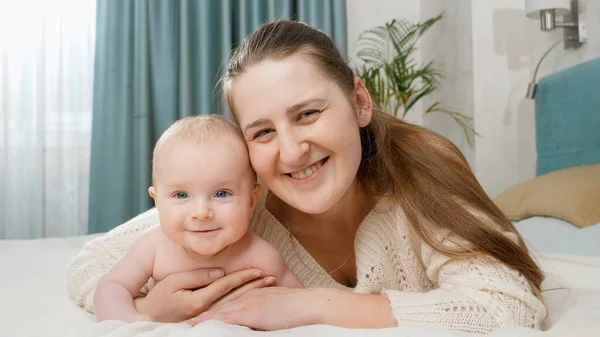 Glückliche Mutter umarmt ihr lächelndes Baby, während sie mit ihm im Bett liegt. Konzept von Elternschaft, Babybetreuung und Familienglück — Stockfoto