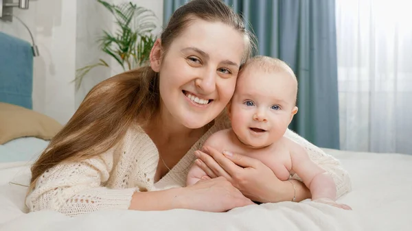 Portret uśmiechniętego dziecka i matki leżących na łóżku i patrzących w kamerę — Zdjęcie stockowe
