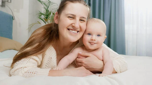 Lächelnder kleiner Junge mit glücklicher Mutter, die im Bett liegt und in die Kamera schaut. Konzept von Elternschaft, Babybetreuung und Familienglück — Stockfoto