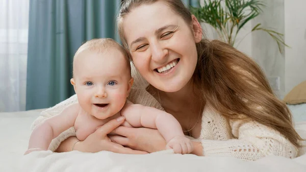 Portret uśmiechniętej szczęśliwej matki obejmującej swojego synka w łóżku rano. Pojęcie rodzicielstwa, opieki nad dziećmi i szczęścia rodzinnego — Zdjęcie stockowe