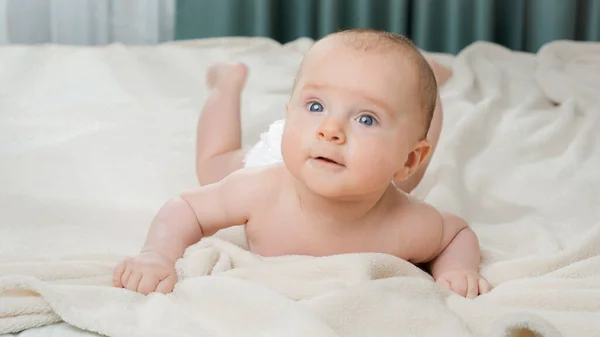 Retrato de lindo bebé con ojos azules acostado sobre una manta blanca en el dormitorio — Foto de Stock