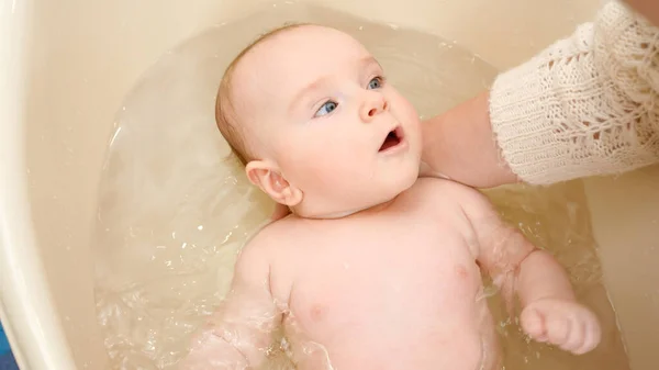 Großaufnahme einer Mutter, die den Babykopf beim Waschen in der Badewanne stützt. Konzept der Kindererziehung, Babypflege und Gesundheitsfürsorge — Stockfoto