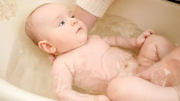 Nettes Baby schaut Mutter beim Waschen in Plastikwanne an. Konzept der Kindererziehung, Babypflege und Gesundheitsfürsorge. — Stockfoto