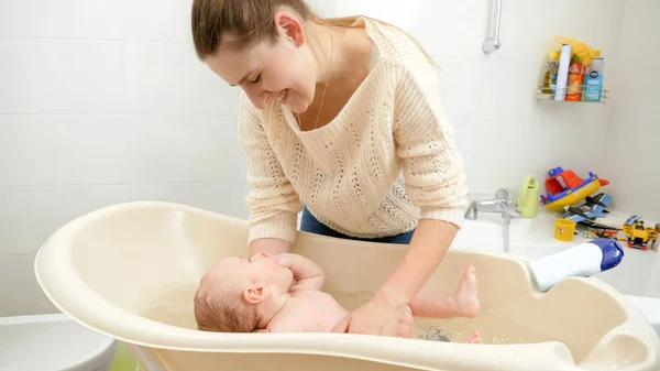 Feliz madre sonriente lavando a su pequeño hijo en el baño. Concepto de higiene, cuidado del bebé y atención sanitaria — Foto de Stock