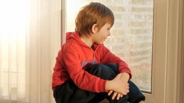 Niño sonriente sentado en la ventana y disfrutando del atardecer — Foto de Stock