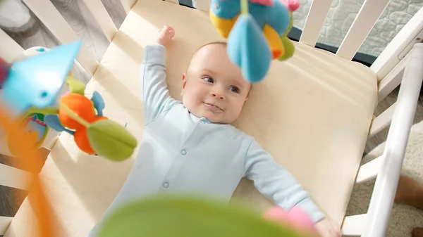 Cute little baby leżące w łóżeczku i patrząc na wiszące kolorowe zabawki. Koncepcja edukacji, opieki zdrowotnej i rozwoju dzieci. — Zdjęcie stockowe