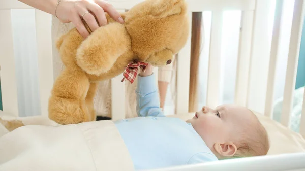 Roztomilý chlapeček dívající se na plyšového medvídka v náručí matky. Pojem rodičovství, rodinné štěstí a vývoj dítěte — Stock fotografie