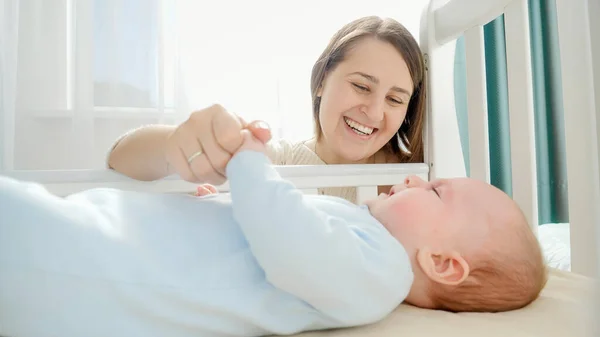 Sorridente madre premurosa e amorevole accarezzando il suo bambino nella culla. Concetto di genitorialità, felicità familiare e sviluppo del bambino — Foto Stock