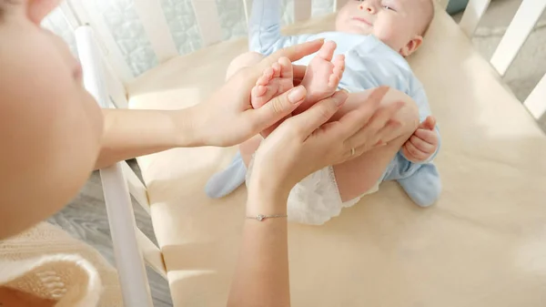 Mujer feliz mirando a su bebé tumbado en la cuna y besando pequeños pies. Concepto de paternidad, felicidad familiar y desarrollo del bebé — Foto de Stock