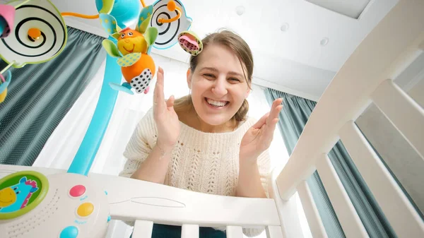 Retrato de mãe sorridente feliz brincando de esconde-esconde com seu bebê deitado no berço. Conceito de parentalidade, felicidade familiar e desenvolvimento do bebê. — Fotografia de Stock