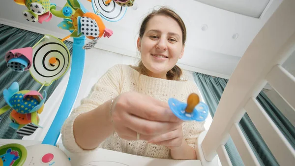 POV of mother giving pacifier and stroking her little baby lying in wooden crib. Concept of parenting, family happiness and baby development — Stock Photo, Image