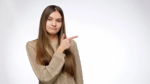 Självsäker leende flicka som pekar med pekfingret på sidan. Placera din produkt eller objekt. Mall för reklam. — Stockfoto