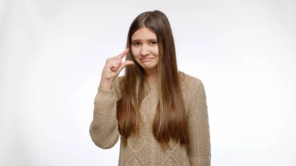 Portrait of sceptic girl showing small size with hand over white studio background — Stock Photo, Image