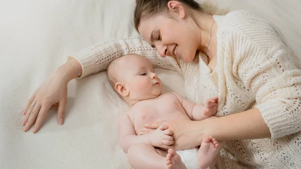 Fiatal anya fekszik a kisfiával az ágyban, és gyengéden simogatja. — Stock Fotó