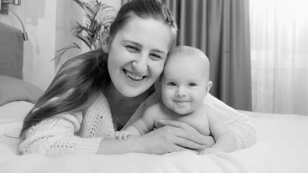 Retrato en blanco y negro del feliz bebé sonriente y mamá acostada en la cama —  Fotos de Stock