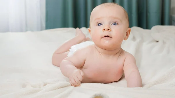 Retrato de lindo bebé con ojos azules acostado en la cama y mirando en la cámara. — Foto de Stock