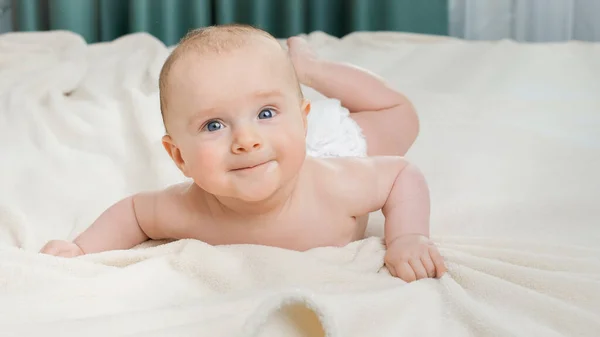 Netter kleiner Junge mit blauen Augen liegt auf dem Bett und krabbelt in Richtung Kamera. — Stockfoto