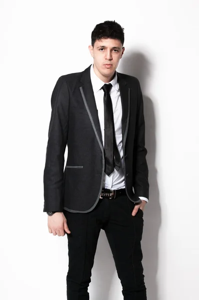 Elegant man in black suit leaning against white wall at studio — Stock Photo, Image