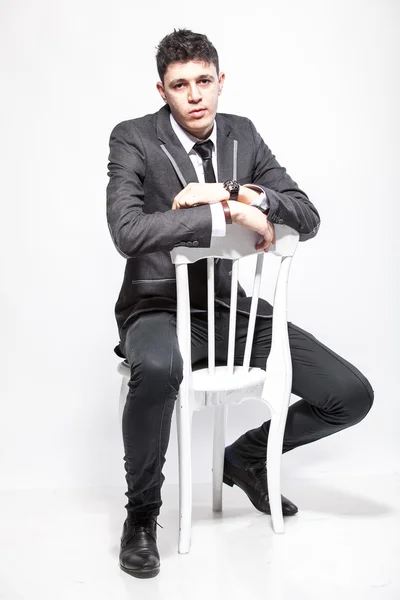 Брюнетка мужчина в костюме и галстуке сидя на белом стуле — стоковое фото