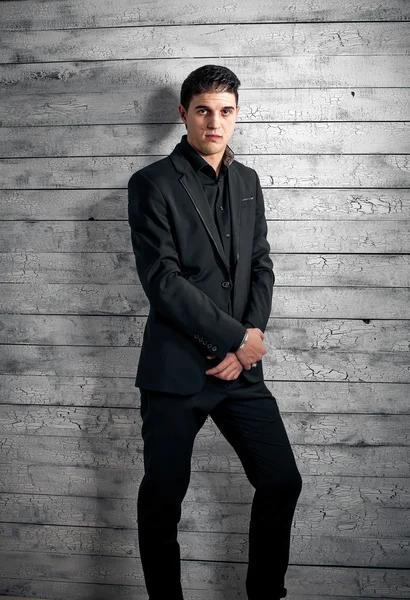 Brunette man in black suit leaning against white leaning wall — Stock Photo, Image