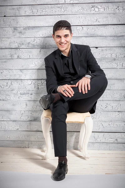 Portrait of smiling latin man sitting on chair against wooden wa — Stock Photo, Image