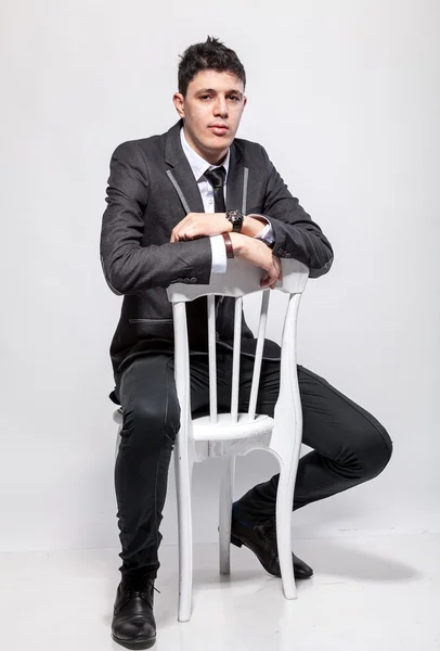 Elegant man in suit sitting on wooden chair at studio — Stock Photo, Image