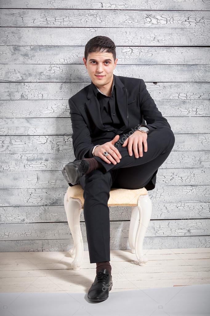 Man in suit sitting on chair with legs crossed at studio Stock Photo by