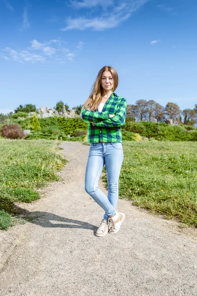 Ung kvinna i skjorta och jeans står på väg på park — Stockfoto