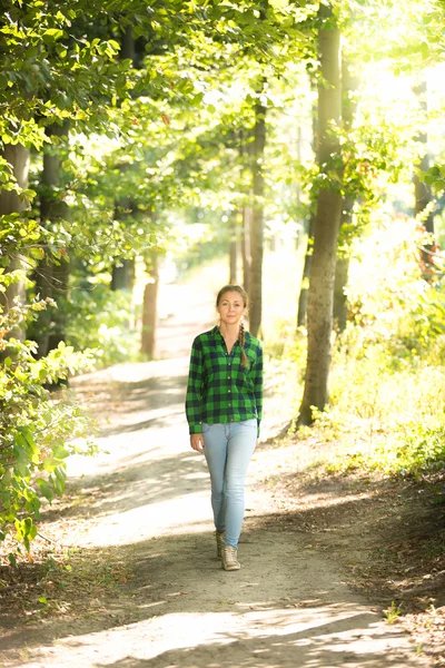 Frau in Hemd und Jeans spaziert an sonnigem Tag im Wald — Stockfoto