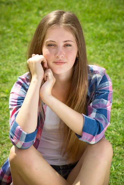 Vacker student tjej i skjortan sitter på gräset — Stockfoto