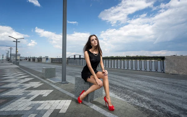 Slanke vrouw zitten op straat tegen blauwe hemel — Stockfoto