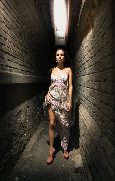 Brunette woman in long dress walking between two brick walls — Stock Photo, Image